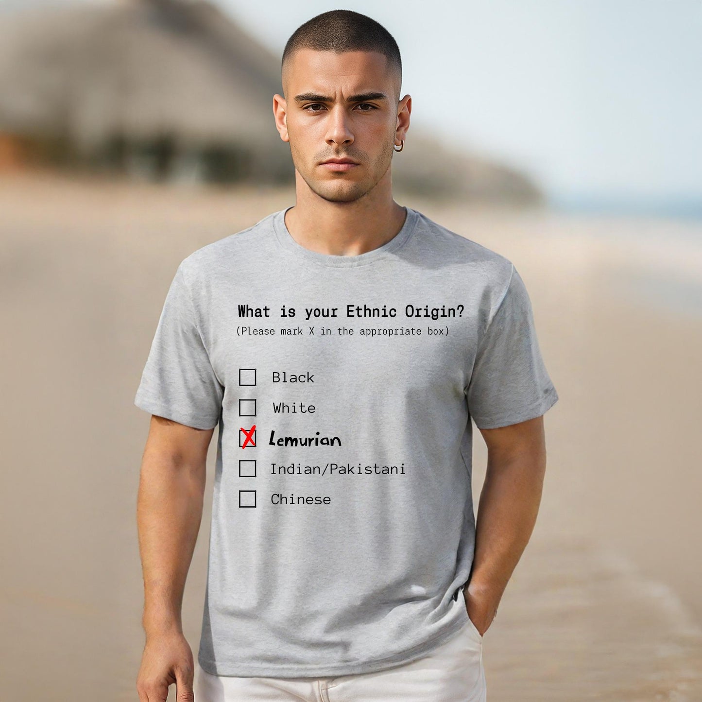 Man wearing a gray t-shirt with a humorous ethnic origin quiz on a beach.
