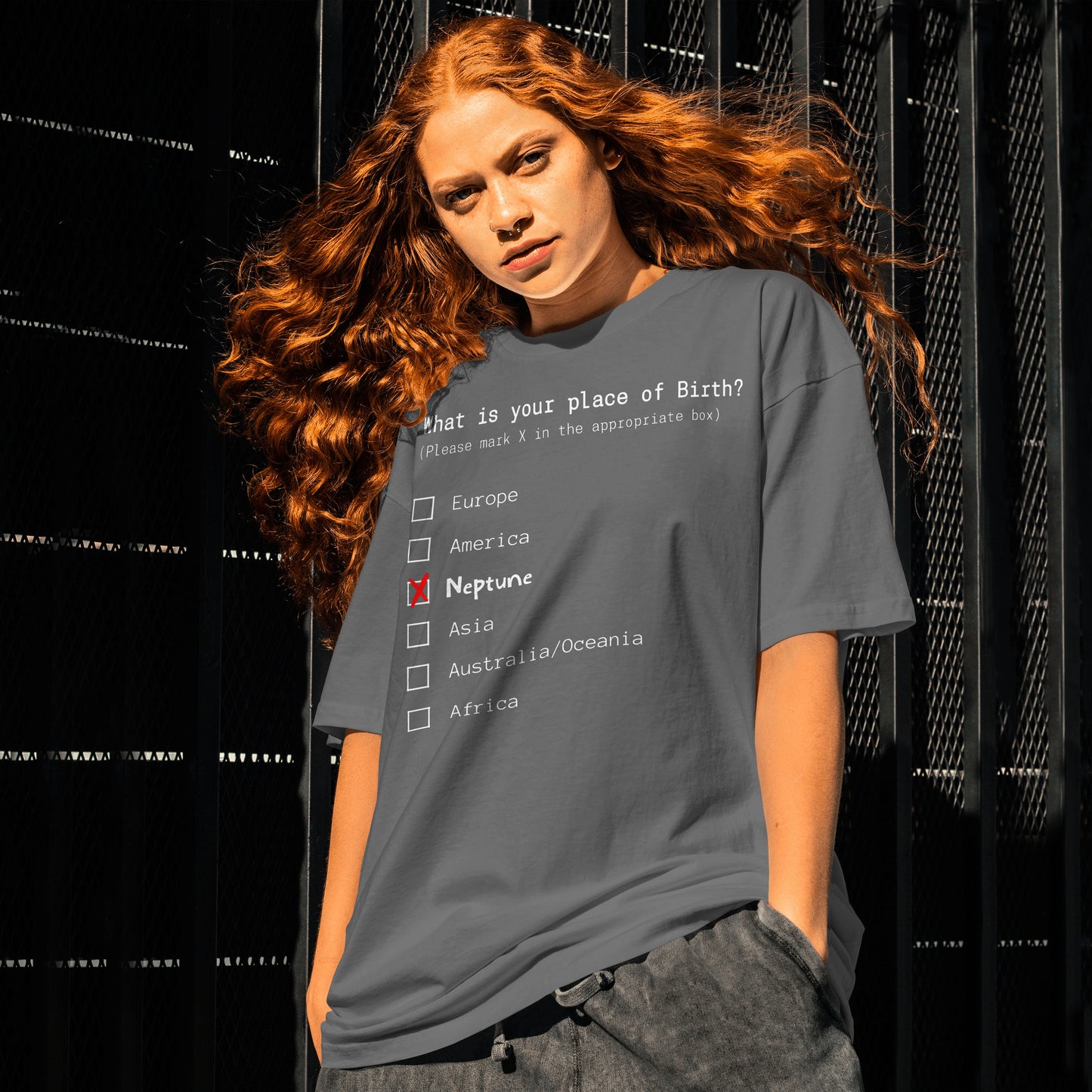 Person wearing a t-shirt with a humorous 'place of birth' quiz design against a black background.