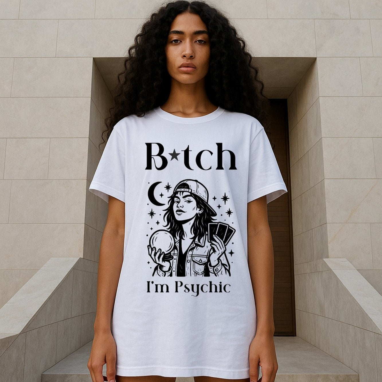 Model wearing a white Bitch I'm Psychic T-shirt with a graphic of a girl in baseball cap holding a Crystal Ball in one hand, and Tarot cards in the other hand.