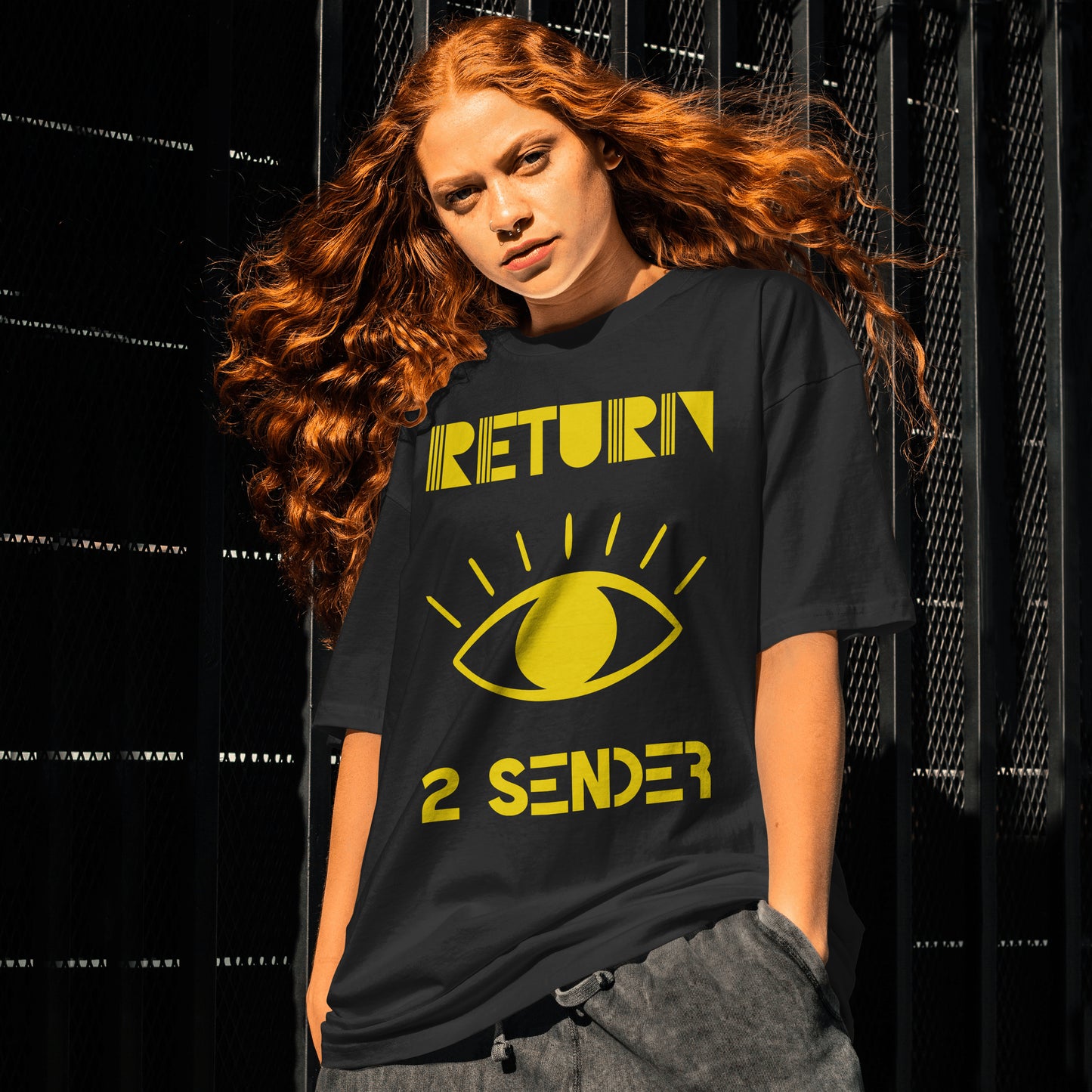 Model wearing a Black T-shirt featuring the slogan Return 2 Sender in Yellow with a large Yellow evil eye in the centre.